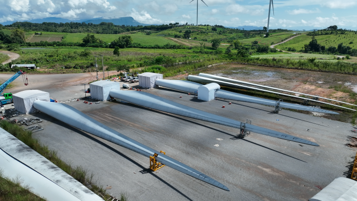 Three rotor blades are seen on the ground within the wind park. The root of the rotor blades have each been placed in a working environment, a tent seen on the picture, where work will be conducted: one tent will drill out bushing, the next tent will insert the new bushings and the third tent will ensure the whole area with wth new bushings is alligned
